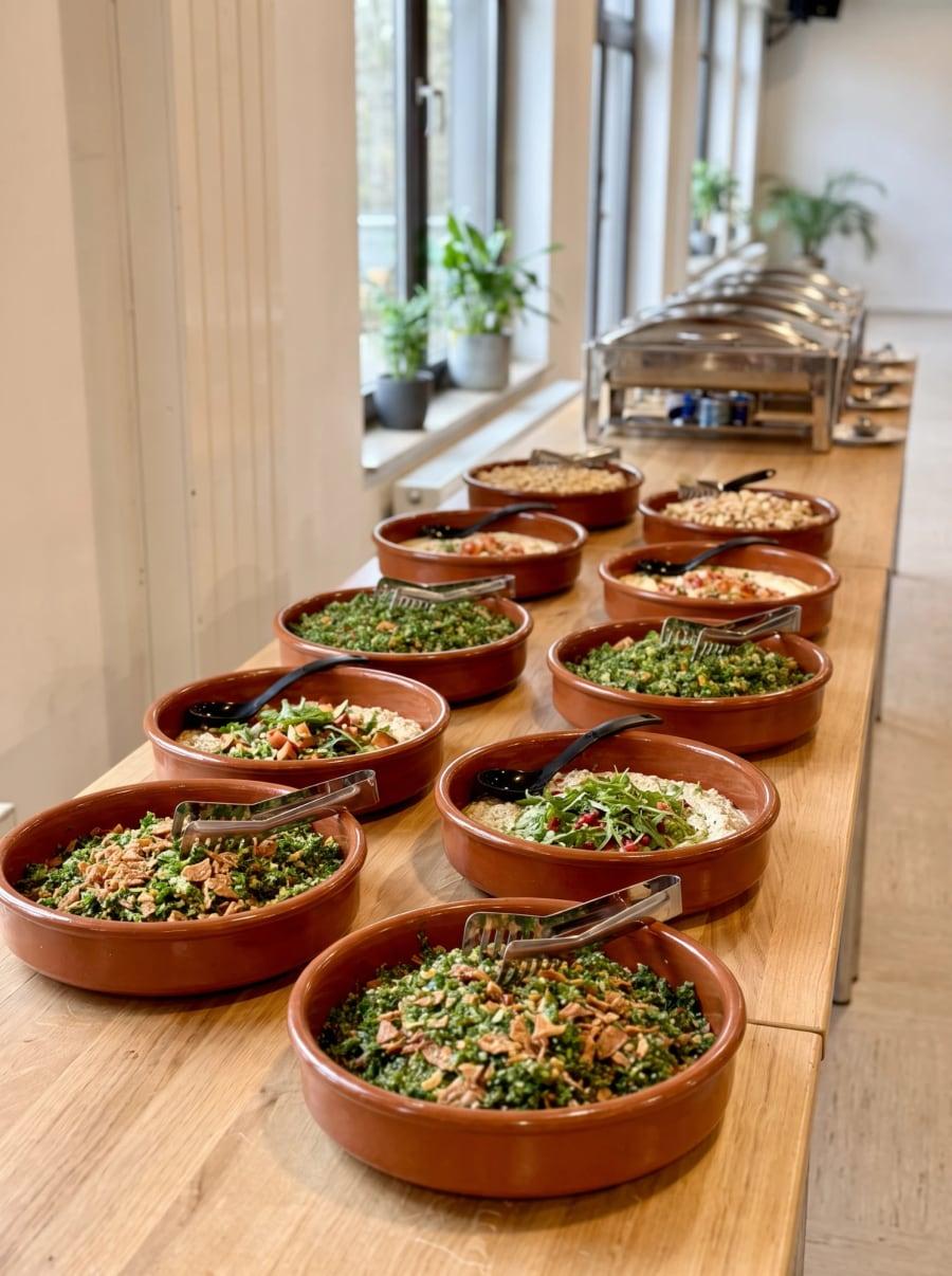Salate und Dips in Tonschalen, dahinter Chafing Dishes